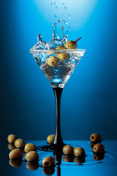 Martini with green olives on a wet table.