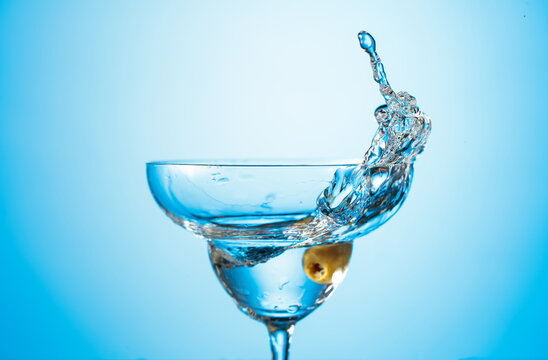 Clear martini glass with green olive in motion.