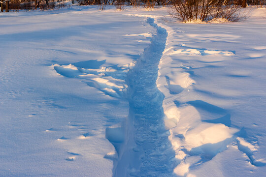 Narrow beaten path through deep untouched white snow in a field at sunset, peaceful winter landscape with shadows across the pristine cold ground during a crisp frosty evening walk
