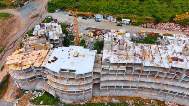 Top view of apartment complex construction with tower crane. High angle view of reinforced concrete building structure with formwork, scaffolding, and yellow tower crane at work.
