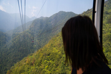 Person riding a gondola cabin, enjoying mountain and forest views © BUDDHA