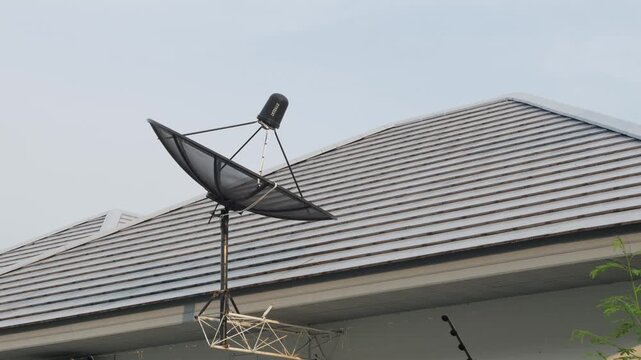 Satellite dish antenna mounted on rooftop of residential house against blue sky with wispy clouds telecommunication technology
