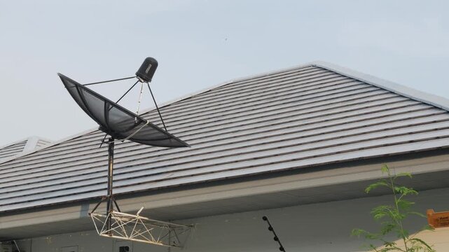 Satellite dish antenna mounted on rooftop of residential house against blue sky with wispy clouds telecommunication technology
