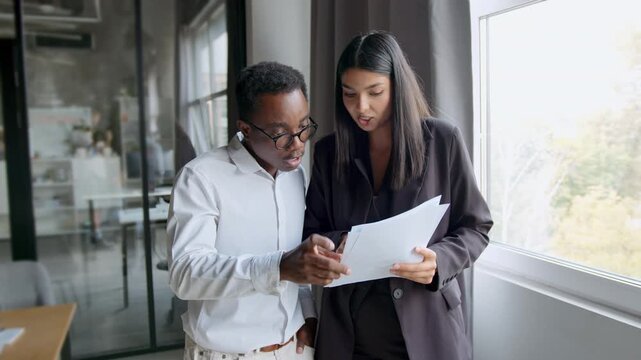 Woman teaches new employee in office about tasks using papers while looking at documents during training phase in a startup environment