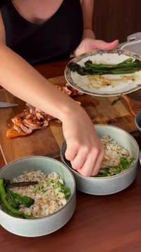 Woman Placing Broccolini into Salmon Rice Bowls Healthy Food Preparation Close Up Meal Assembly Fresh Ingredients Culinary Kitchen Cooking Process Gourmet Nutrition Bowl 4K Video