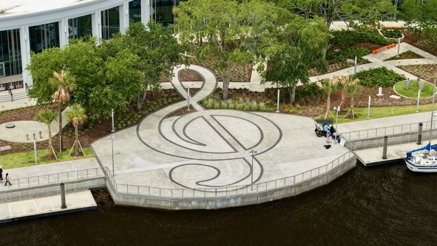 Aerial view of the treble clef design at Riverfront Plaza with trees and people near a docked boat on the St. Johns River in Jacksonville, Florida, United States.