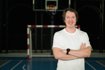 Obraz premium Smiling athletic Caucasian man in his late 30s posing with arms crossed on horizontal outdoor sports court at night
