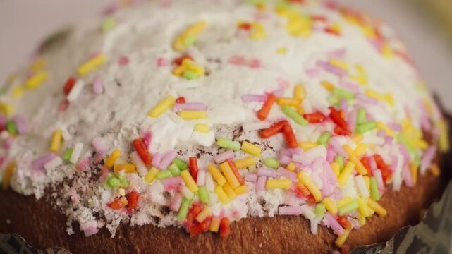Easter cake topped with sugar icing and decorated with colorful sprinkles. Traditional kulich decoration, close-up. High quality 4k footage