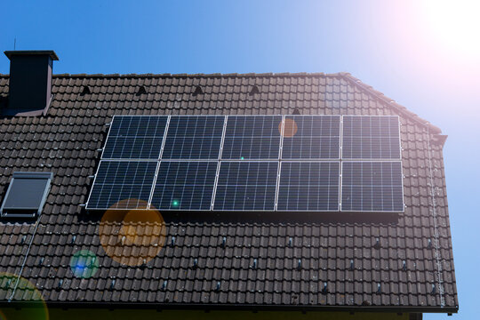 solar panels roof house sun lens flare photovoltaic cells installation on tiled rooftop alternative energy system blue sky background concept of green energy, ecology, sustainable architecture