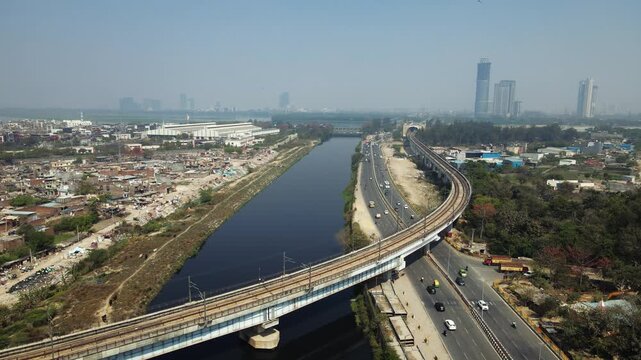 Aerial view of traffic time-lapse in Delhi city featuring busy roads alongside a metro track running parallel to a river.	