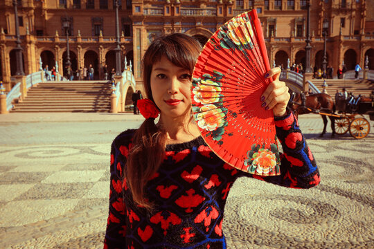 Beautiful asian woman holding Spanish  fan in front of Plaza de Espana in Seville, Spain during her vacation