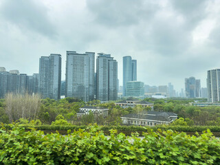 Fototapeta premium Modern Hangzhou skyline towers rising above green parkland under an overcast spring sky, China