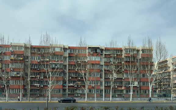 Residential apartment blocks and leafless trees along a wide urban road in Beijing, China. Cloudy sky