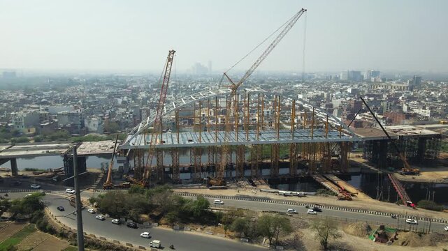 Aerial drone view of an under-construction arch bridge in Delhi, showcasing large-scale infrastructure development. Modern construction techniques, rapid urbanisation and connectivity in India city.