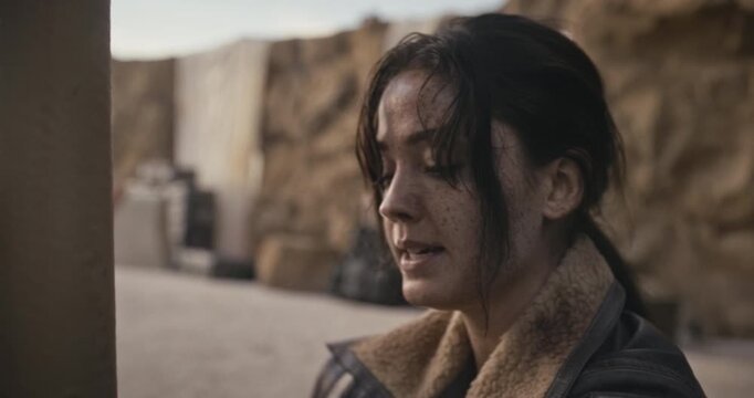 Bound, beat up woman in sci-fi desert area talking to someone off screen - closeup shot