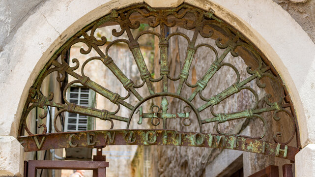Wide view of an old decorative wrought iron grille above a historic gate in Kotor Old Town, Montenegro, with narrow stone street and Mediterranean architecture background