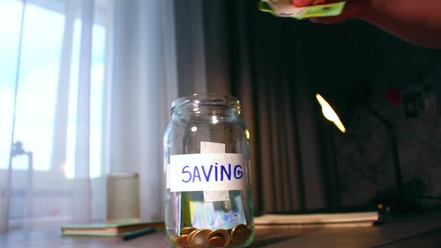 Close up of cash being added to transparent money jar. Represents traditional saving methods and conscious money management for future security