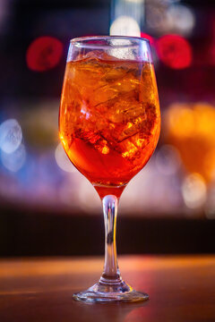 An aperol spritz drink on a glass at a lively bar during the evening with defocused background