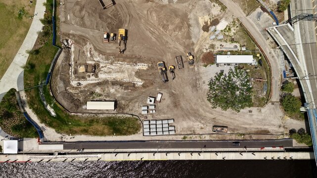 Aerial view of the Riverfront Plaza construction site featuring heavy machinery, excavators, and concrete materials along the waterfront in Jacksonville, Florida, United States.