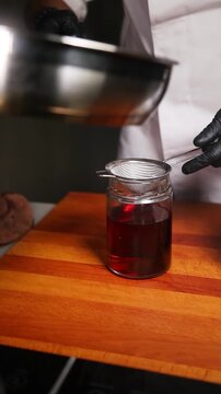 Chef colando aceite de jam&oacute;n ib&eacute;rico en un frasco de vidrio. Chef profesional filtrando la grasa de jam&oacute;n derretida en un frasco. Cocina artesanal espa&ntilde;ola, proceso tradicional.