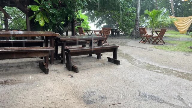 Wooden tables and chairs at a beach cafe during a rainstorm. Mahe, Seychelles, Ance Major beach. Tropical rain on the beach. Rainy season