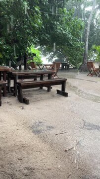 Wooden tables and chairs at a beach cafe during a rainstorm. Mahe, Seychelles, Ance Major beach. Tropical rain on the beach. Rainy season
