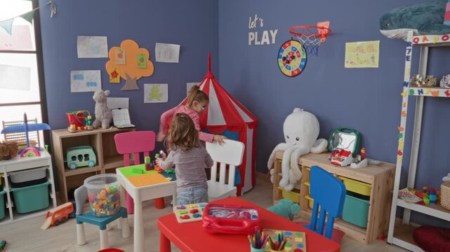 Girl arranging toy blocks with hands by red striped tent and stuffed octopus inside children's playroom building; childhood joy.