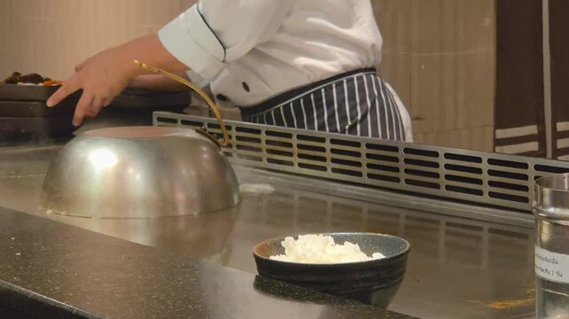 Teppanyaki chef pouring water next to a metal dome cover on a hot grill