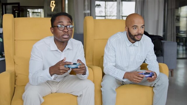 Two Black men in white shirts play a game console in an office. They show intense passion and reactions during their break, with one man eventually celebrating victory with excitement and joy