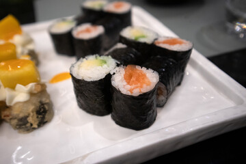 Assortimento di sushi maki giapponesi con salmone e avocado avvolti in alga nori serviti su un piatto bianco © Ilarialapreziosa