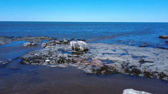 Drone footage orbiting a large erratic rock on the rocky shoreline of Saint-Ulric-de-Matane during spring low tide on the scenic Gasp&eacute; Peninsula, Quebec, Canada.