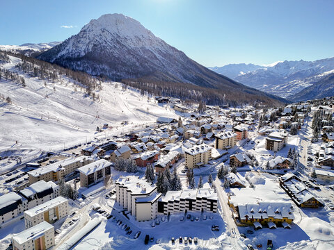 Aerial view of the snow-covered alpine village and ski slopes of Montgenevre with hotels and chalets under a clear blue sky Montgenevre, Provence-Alpes-Cote d, France.