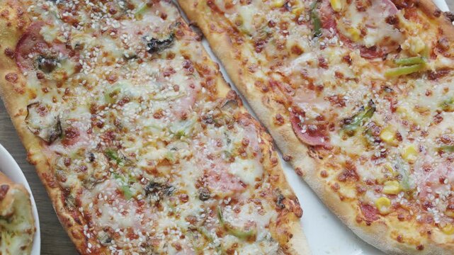 Close-up of sliced rectangular mixed pizza with rich toppings on wooden board