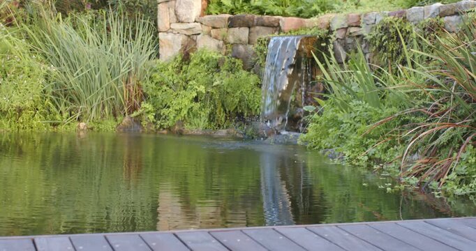 Camera panning over wooden deck as stone spillway feeding pond and making ripples for circulation