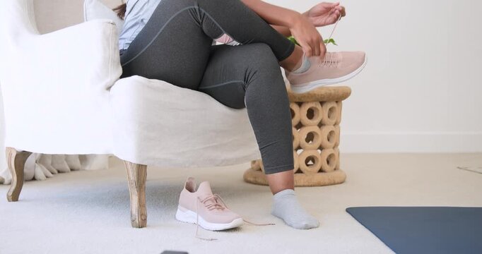 African American woman in leggings putting on pink sneakers tying laces preparing for run at home