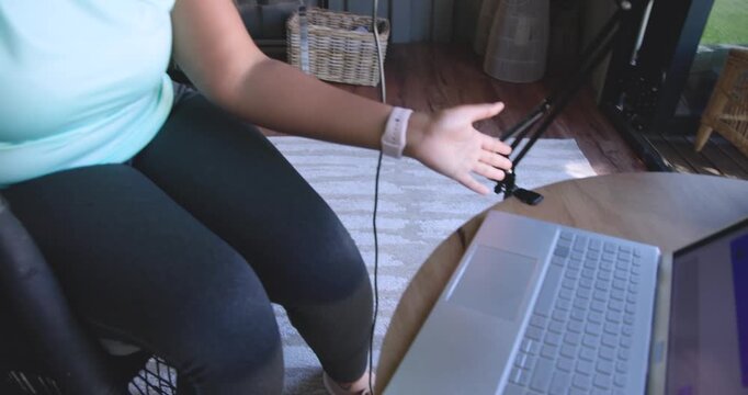 Greeting camera African American woman reaching laptop, speaking into mic, recording in home studio