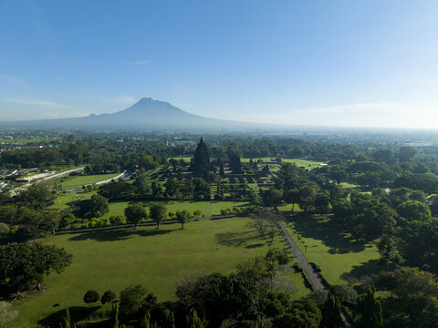 Aerial view of Prambanan Temple surrounded by lush green lawns and trees with Mount Merapi volcano in the background Kecamatan Prambanan, Daerah Istimewa Yogya, Indonesia.
