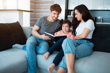 Obraz premium Family at home reading a book. Adult brother and sister reading a book to little sister. Young parents and daughter