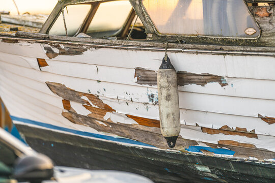 Peeling hull paint and hanging fender on old boat illustrating wear maintenance and neglect.