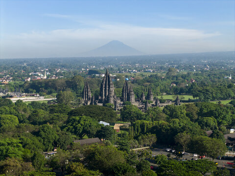 Aerial view of Prambanan Temple complex with its towering stone spires surrounded by lush trees and Mount Merapi in the distance in Kecamatan Prambanan, Daerah Istimewa Yogya, Indonesia.