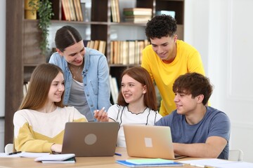 Fototapeta premium Group of students studying with laptops and notebooks at wooden desk in classroom