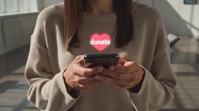 A woman's hands are holding a smartphone, with a heart and the text Donate on the screen.