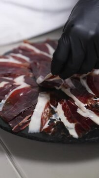 Chef cortando jam&oacute;n ib&eacute;rico y emplatando. Chef profesional cortando y colocando lonchas de jam&oacute;n ib&eacute;rico en un plato. Cocina gourmet espa&ntilde;ola.