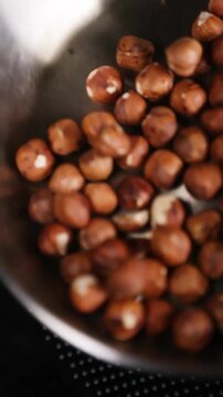 Primer plano de avellanas tostadas en sart&eacute;n de acero inoxidable. Avellanas tost&aacute;ndose en sart&eacute;n de acero. Proceso culinario artesanal, t&eacute;cnica de preparaci&oacute;n de ingredientes gourmet.