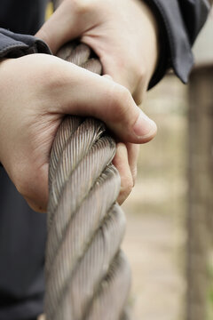 Hands grip thick, twisted steel rope firmly