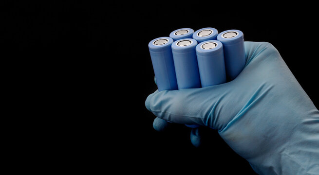 Gloved hand holds blue 18650 lithium-ion battery packs for electrical appliances and devices on black background with copy space.