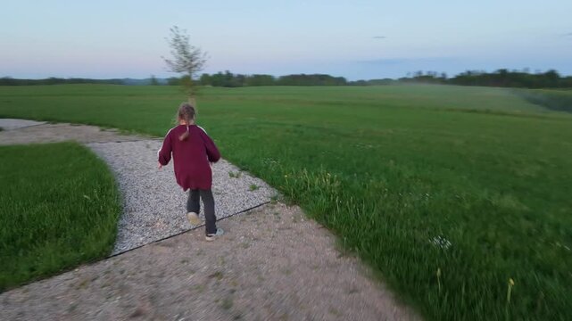 A drone footage of a girl running away from a drone. The action takes place outdoors, in a tourist attraction place - a watchtower built on a hill with a symbolic sun wheel made from cobble stones. 