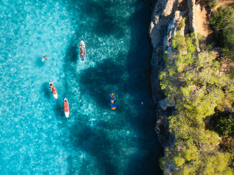 Aerial drone view of colorful kayaks, rocky coastline, green trees and crystal clear turquoise water. Summer adventure in Mallorca, Balearic Islands, Spain. Mediterranean sea. Top down view of canoes