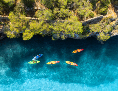 Aerial drone view of colorful kayaks, rocky coastline, green trees and crystal clear turquoise water. Summer adventure in Mallorca, Balearic Islands, Spain. Mediterranean sea. Top down view of canoes