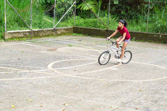 Latina girl gaining speed while riding bicycle on an outdoor concrete soccer court in park
